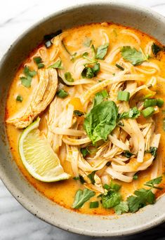 a white bowl filled with noodles and garnished with cilantro, parsley and lime