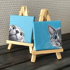 two small paintings of cats on easels with one cat looking at the camera and another staring up