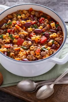 a large white bowl filled with pasta and sausage soup on top of a wooden cutting board