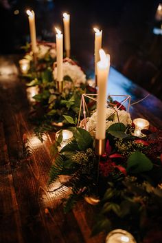 candles are lit on a long table with greenery and flowers in front of it