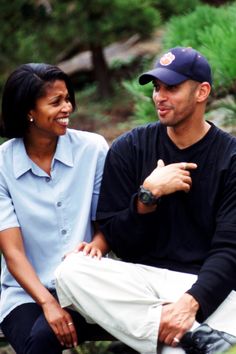 a man and woman sitting next to each other on a bench in the woods talking