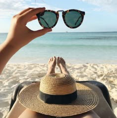 a person laying on top of a sandy beach next to the ocean wearing sunglasses and a straw hat