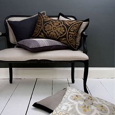 a chair with some pillows on it in front of a gray wall and white floor