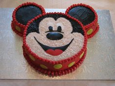 a mickey mouse cake with red and yellow icing on it's face, sitting on top of a table