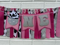 pink and black banner with letters on it hanging from a line in front of a white brick wall