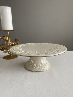 a white cake plate sitting on top of a table next to a candle and a vase