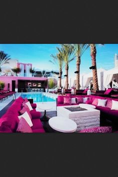 an outdoor lounge area with pink couches and tables next to a pool in front of palm trees