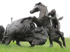 two statues of people riding horses in the grass