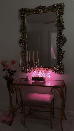 a table with a mirror, stool and candles on it in front of a pink light