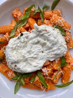 a white plate topped with pasta covered in sauce and cheese next to green leafy garnish