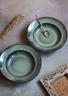 two plates with spoons sitting on top of each other next to a woven place mat