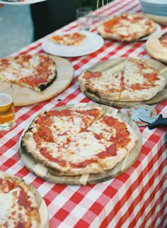 several pizzas sitting on top of a red and white checkered tablecloth covered table