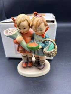 two figurines sitting on top of a table next to a box with a basket