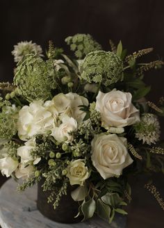 a vase filled with white flowers on top of a wooden table covered in greenery