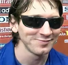 a man wearing sunglasses and smiling at the camera with many stickers on his wall behind him