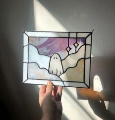 a hand holding up a stained glass window with a ghost on it's side