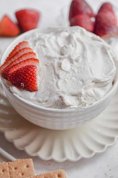 a white bowl filled with whipped cream and strawberries next to crackers on a plate