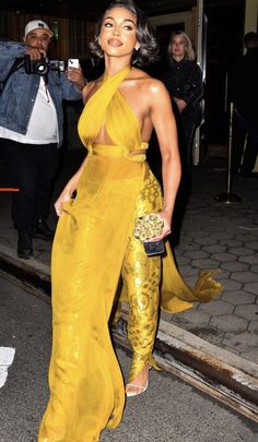 a woman in a yellow dress is walking down the street with her hand on her hip