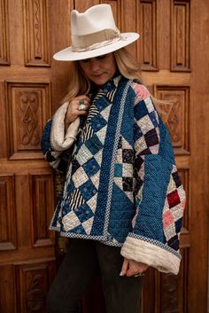 a woman standing in front of a wooden door wearing a white hat and jacket with patches on it