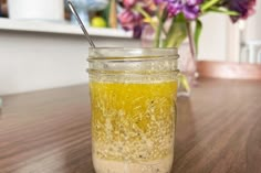 a jar filled with yellow liquid sitting on top of a wooden table next to flowers