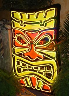 an illuminated tiki mask in front of some plants