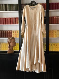 "The best silk satin fabric of a medium to heavyweight with a strong sheen.  It's in a buttery cream colour. The bodice is quite plain with five pintuck features at the waist. It's at the hip and skirt area that this gown comes into its own.  Diagonal design lines at the drop waist with a pointed design on one side.  That curved design line then becomes an upward wave in the hemline.   A full flared skirt that dips at the back to a slight train. The sleeve cuffs are pointed with press studs clos Fitted Satin Finish Dress For Wedding Night, Fitted Cream Satin Evening Dress, Cream Satin Fitted Evening Dress, Formal Off White Satin Dress, Off White Satin Formal Dress, Satin A-line Evening Dress For Wedding, Cream Satin Gown With Fitted Bodice, A-line Satin Evening Dress For Wedding, Elegant Cream Gown For Wedding Night