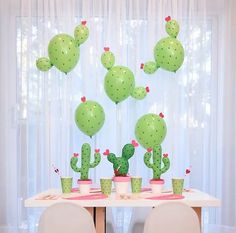 a table topped with lots of green balloons and potted cacti on top of it