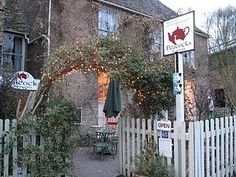 an outside view of a restaurant with tables and umbrellas on the front lawn, next to a white picket fence