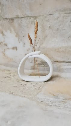 a white vase sitting on top of a stone wall next to a plant in it