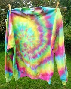 a colorful tie - dyed shirt hanging on a clothes line in front of some bushes