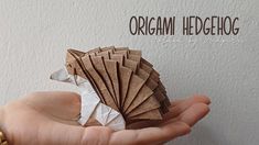 a hand holding an origami hedgehog made out of brown and white paper