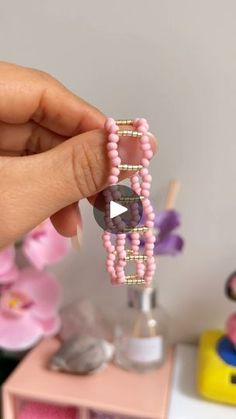 a person holding a pink beaded bracelet in front of a flower vase with flowers on it