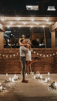 a man and woman kissing in front of candles on the ground with lights strung all around them