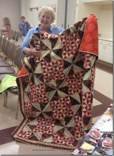 an older woman holding up a quilt in a room