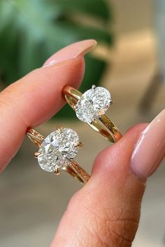 a person holding two diamond rings in their hand, one is yellow gold and the other is white gold