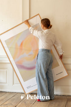 a woman holding up a large painting on the wall