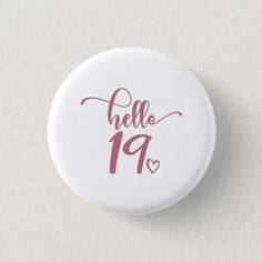 a white button with the words hello 19 printed on it and hearts in pink ink