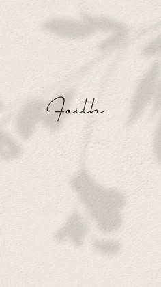 the word faith written in cursive writing on a white wall with shadow from leaves