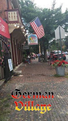 an old brick street with the words german village on it's side and american flags flying in the background