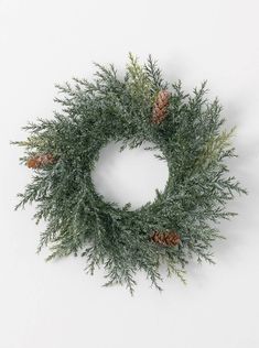 a wreath with pine cones and greenery is shown on a white background in this image