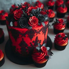 a red and black cake surrounded by cupcakes with roses on top, sitting on a table