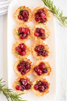 small cranberry tarts on a white plate with rosemary sprigs next to them