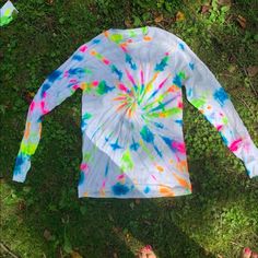 a tie - dyed shirt laying on the ground with someone's feet in the grass