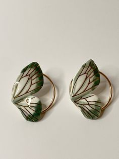 two green and white leaf shaped brooches sitting on top of a white surface