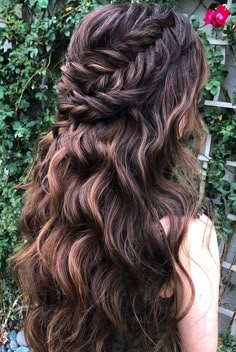 the back of a woman's head with long wavy hair and flowers in the background