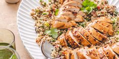 a white plate topped with sliced chicken and couscous next to two glasses of water