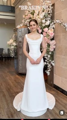 a woman standing in front of a flower display wearing a white dress and posing for the camera