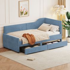 a blue daybed with drawers underneath it in a room next to a rug and potted plant