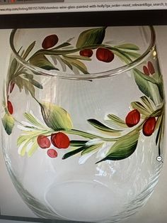 a wine glass painted with red berries and green leaves on the bottom, sitting on a shelf