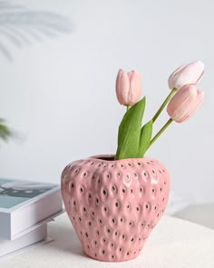 a pink strawberry shaped vase with flowers in it sitting on a table next to a book